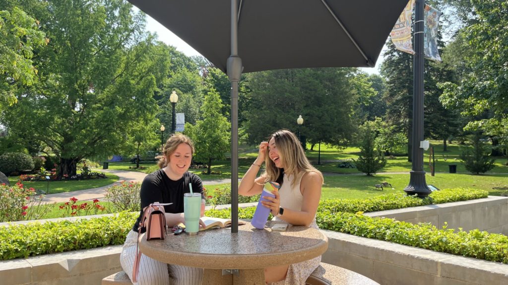 Two women sitting at a table with umbrella in a park
